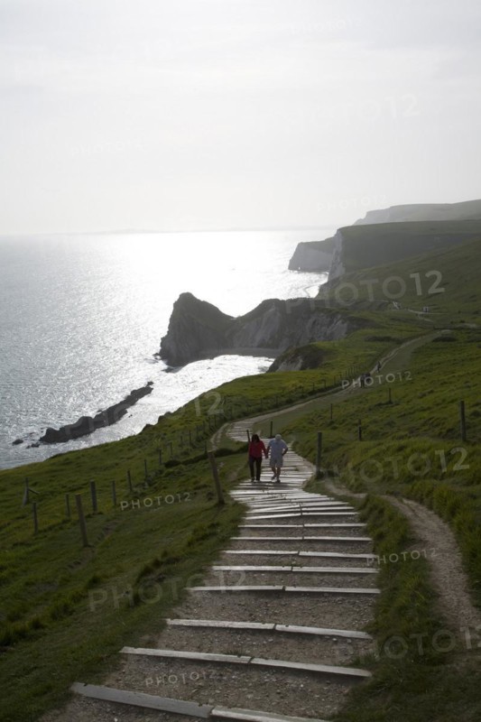 Couple walk up steps from Durdle Door, Jurrassic coast, Dorset, England, United Kingdom