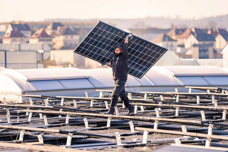 Worker carries solar module on a roof for installation, PV assembly at OBI Baumarkt, Mühlacker, Enzkreis, Germany