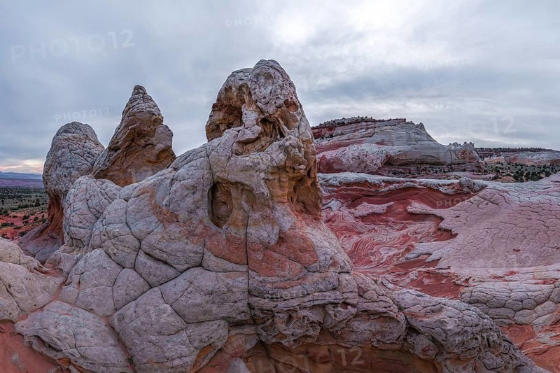 Dramatic landscape of White Pocket, Arizona, featuring intricate rock formations with red and white swirling patterns under a cloudy sky