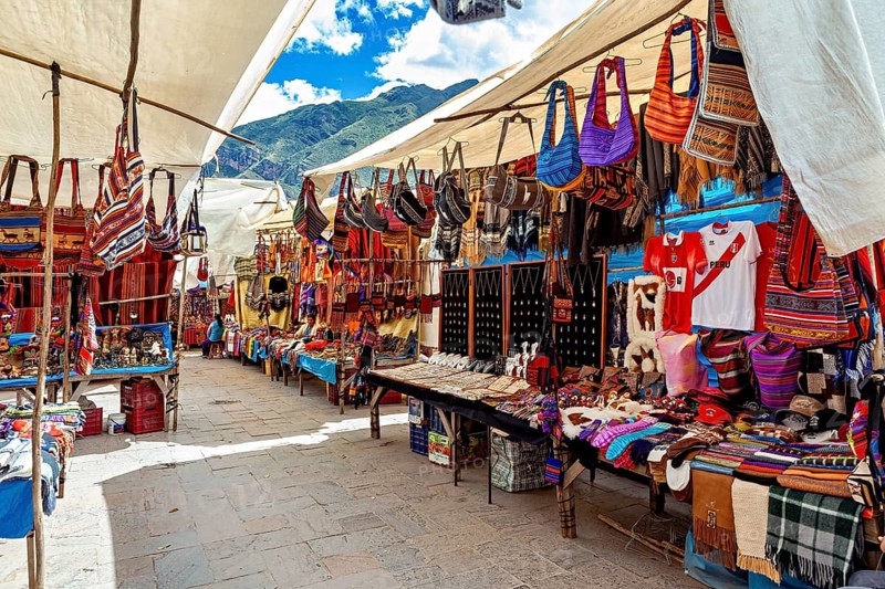Colourful market stalls with traditional Peruvian textiles and bags under blue skies, the city of Ollantaytambo in the Andes of Peru