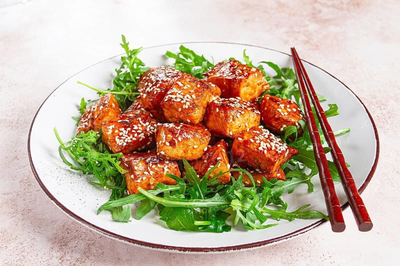 Fried salmon slices, teriyaki with sesame seeds, with arugula salad, top view