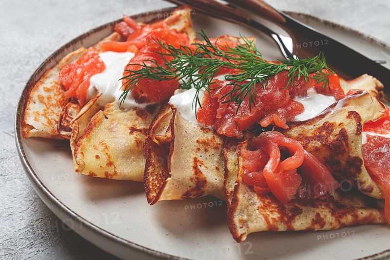 Delicious pancakes with salmon and sour cream, breakfast, on a plate, rustic style, with cutlery