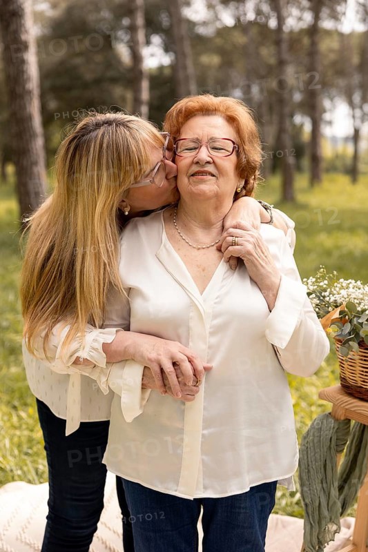 A touching moment between a mother and daughter, captured in a serene outdoor setting. The daughter lovingly kisses her mother on the cheek, symbolizing their deep bond and affection