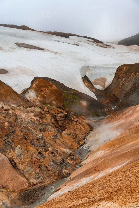 Steaming stream between colourful rhyolite mountains with snowfields, Hveradalir geothermal area, Kerlingarfjöll, Icelandic highlands, Iceland