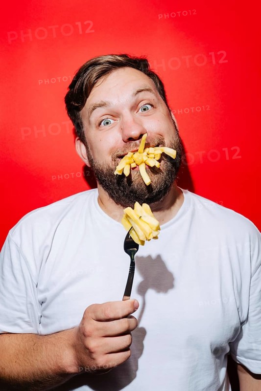 A playful scene featuring fries on a fork and in a man's mouth, against a striking red background. The humorous setup captures a lighthearted barbecue party vibe