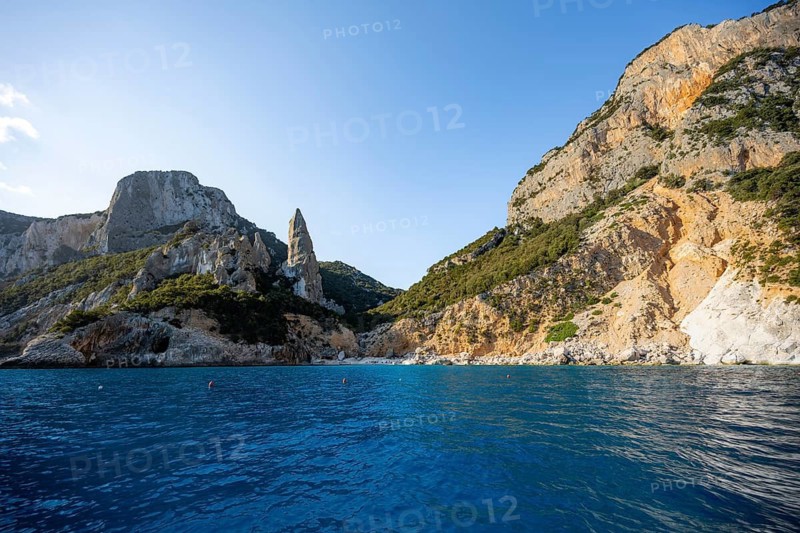 Picturesque rocky coast, cliffs with caves in the morning light, L'Aguglia rock peak, blue sea and Cala Goloritzé beach, Golfo di Orosei, Baunei, Sardinia, Italy