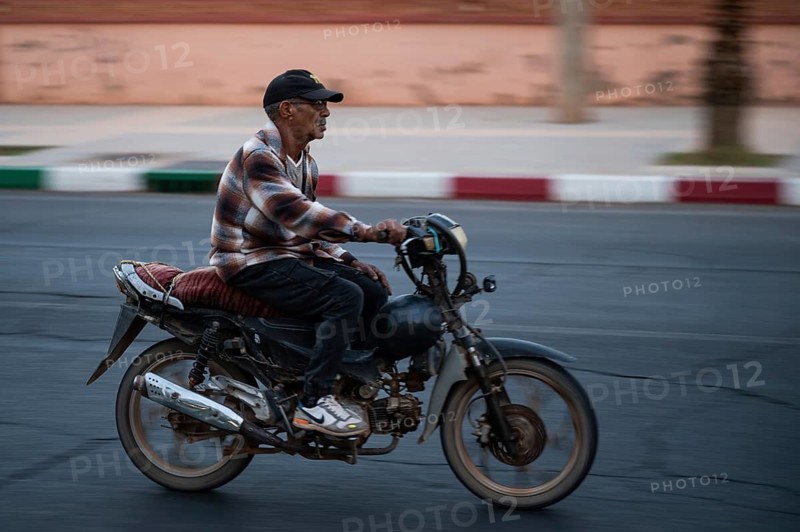Marrakesh, MOROCCO - OCTOBER 5, 2024: Moroccan man riding a scooter on the road. Blurred background due to panning