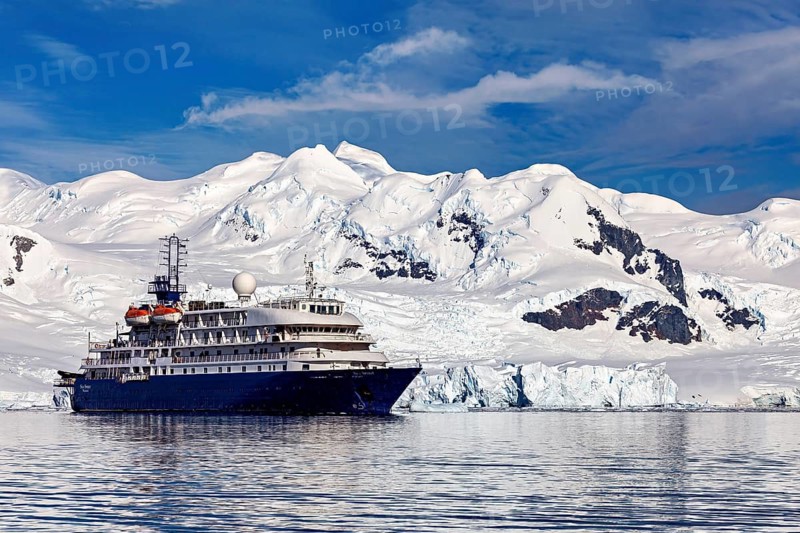A cruise ship in front of a majestic snow-covered mountain range in the icy ocean, cruise ship underway in the Southern Ocean in Antarctica