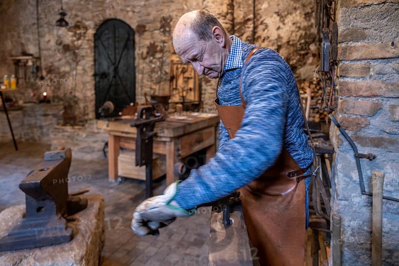 In the Salzburg region of Austria, an elderly blacksmith is immersed in his craft, maintaining centuries-old traditions in his rustic workshop, filled with tools and history
