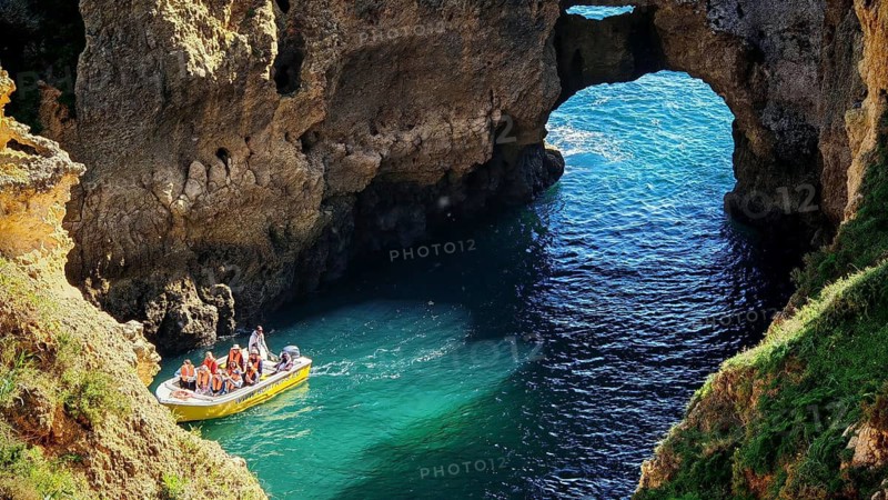 Small boat with tourists in turquoise water in front of an impressive rock formation, rock arch and cave, Ponta da Piedade, Lagos, Algarve, Portugal