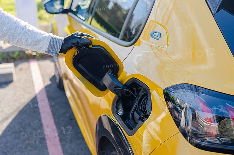 A person in gloves plugs a yellow electric car into a charging station. The scene highlights eco-friendly transportation and the rise of sustainable energy solutions