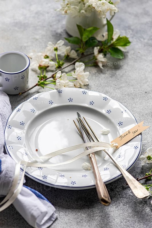 A beautifully arranged table setting featuring a vintage plate, cutlery with a thank you tag, and delicate white flowers. Perfect for weddings or elegant gatherings
