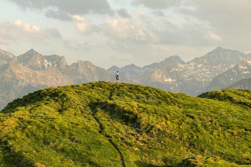 A man pauses on a grassy trail, capturing a moment of serenity with stunning mountainous views in the background. This scene embodies the essence of a calming nature break