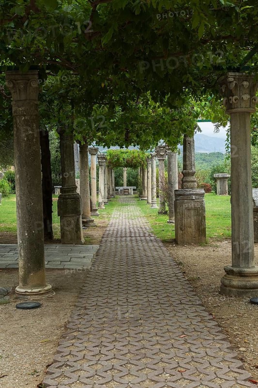 Shade garden with paving stone foot path and pergola covered with live plants and supported by old stone columns at ancient 3rd century Roman ruins of Salona near Solin, Croatia