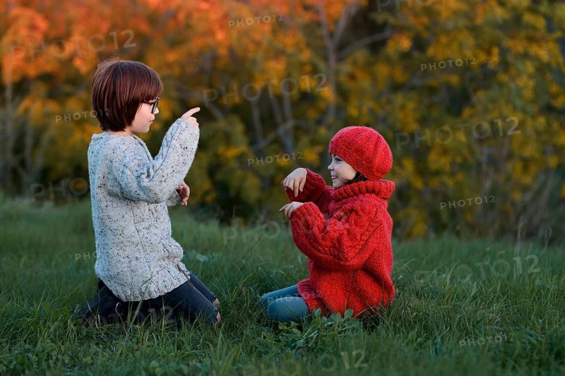 A girl and a boy, siblings, are enjoying a playful day in an autumn park, surrounded by vibrant fall foliage
