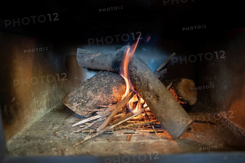 Close-up view of burning wood logs and kindling inside a wood burning stove, capturing the vibrant flames and glowing embers