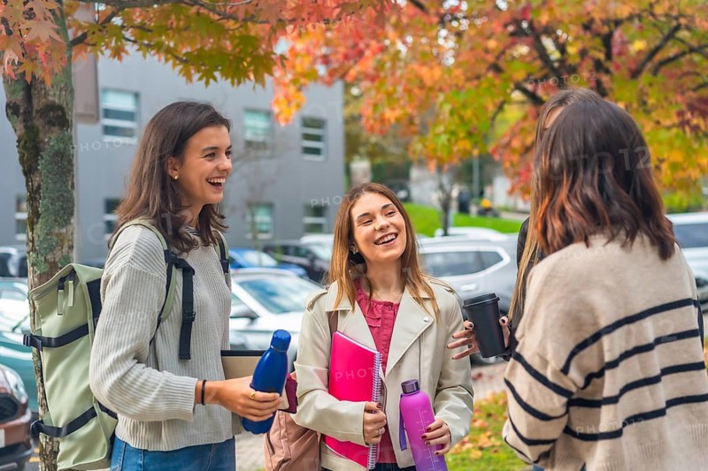 Diverse group of young women students laughing and chatting on a university campus in autumn, relaxed and social, enjoying friendship and fresh air between classes