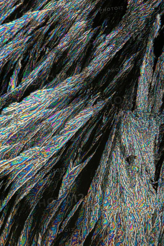 Microscopic view of Vitamin C crystals, presenting a spectacular array of iridescent blues, greens, and oranges intertwined in a complex, fibrous texture