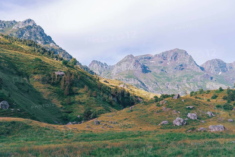 Scenic view of the lush green slopes and rocky peaks of the Ibones de Anayet in Huesca, Spain. The vast landscape under a cloudy sky creates a serene hiking destination