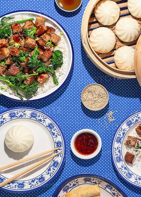 Top view of a traditional Chinese meal featuring steamed buns, tofu, and spring rolls on a blue patterned tablecloth