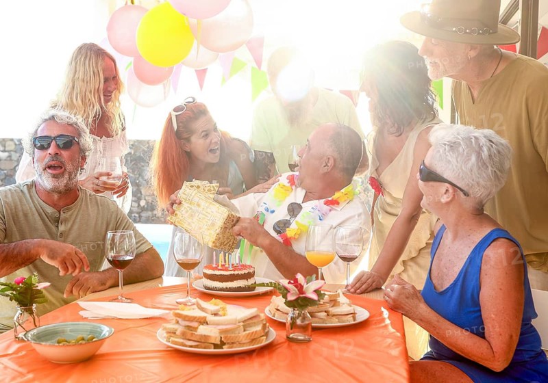 A lively group of friends gathers outdoors to celebrate a birthday. Laughter, gifts, and joy are shared under bright decorations, creating a warm and festive atmosphere