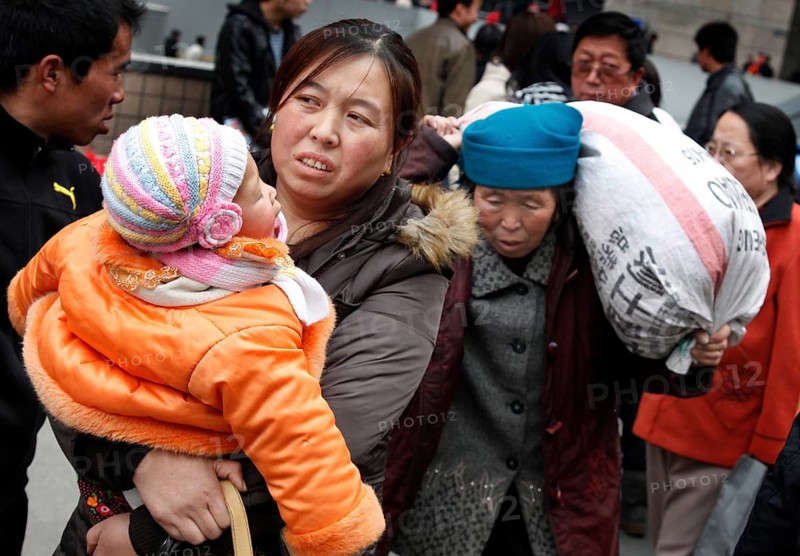Beijing, CHN, 23.02.09 - A Chinese mother carries her child in her arms to the train station, followed by an elderly woman carrying a heavy sack on her shoulders, CHINA