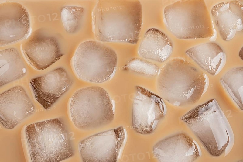 A close-up view of ice cubes floating in a cold brew coffee. The light brown coffee creates a refreshing contrast with the clear ice, evoking a cool, invigorating feeling