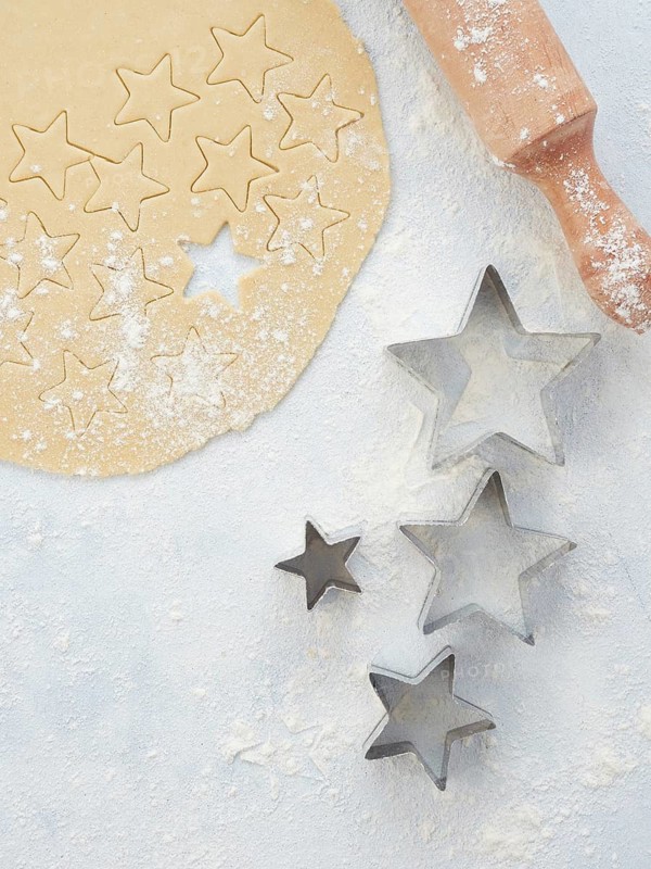 Baking at home, pastry dough with star-shaped cutters of different sizes. Wooden rolling pin and flour sprinkled on the table, seen from above