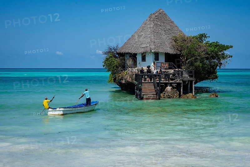 MICHAMVI PINGWE, ZANZIBAR - OCTOBER 19, 2025: the famous Rock Restaurant in Zanzibar at high tide, with a small boat approaching the unique wooden structure built on a coral outcrop