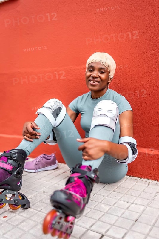 Vertical portrait of a stylish modern african woman smiling sitting on the ground wearing inline skates