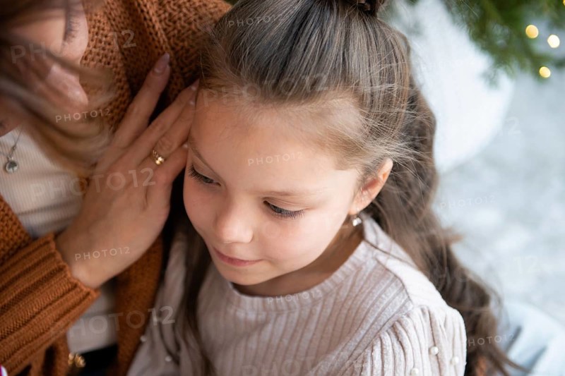 A touching scene captures a young girl looking down, nestled against her unrecognizable mother during Christmas celebrations. The mother is blurred and partially visible, creating an intimate and cozy atmosphere