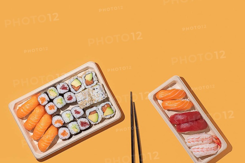 Minimalist overhead shot of sushi takeout boxes on a orange background, featuring nigiri and maki rolls with strong directional lighting