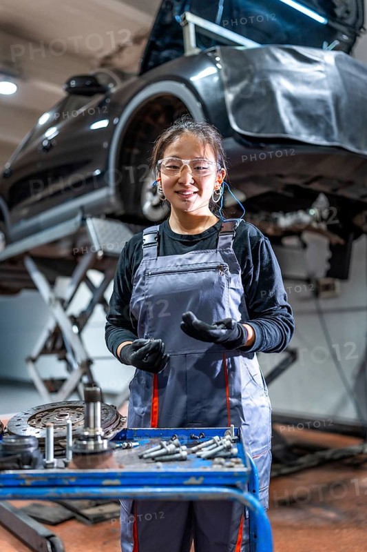 Young female mechanic wearing gloves and safety glasses working on a car in a professional auto repair shop