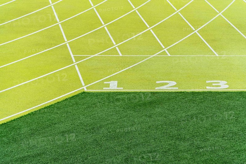 A bright, detailed view of start lines numbered one to three on a green athletics track in an outdoor stadium, symbolizing readiness and competition