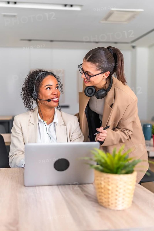 Two female colleagues working together on a project, using a laptop and discussing strategies in a modern workspace