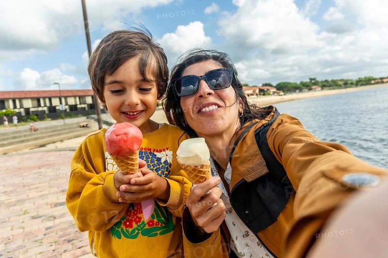 Happy mother and son taking a selfie together, holding ice cream cones while on vacation at the beach, enjoying a sweet treat and sunny weather by the water