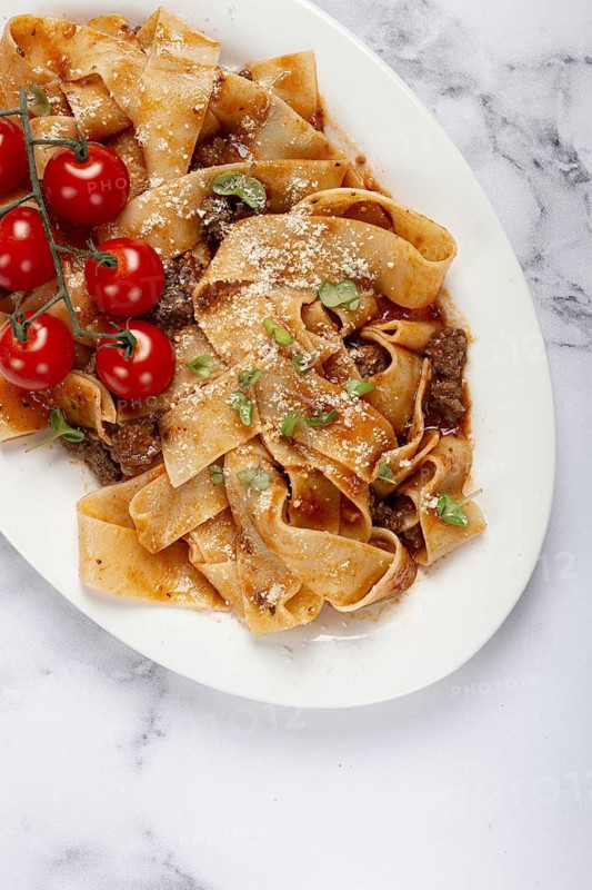Pappardelle pasta with bolognese sauce, topped with parmesan cheese and cherry branch, homemade, no people