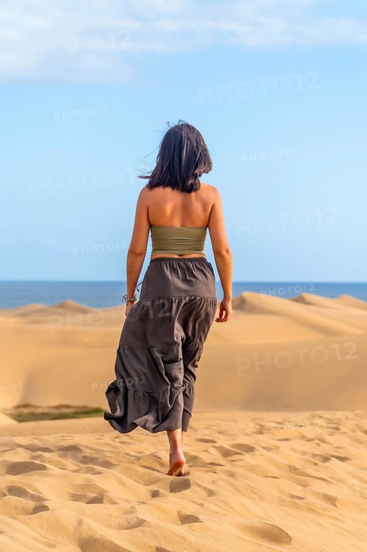 Woman walking barefoot on the sand enjoying the sunny day at maspalomas dunes in gran canaria
