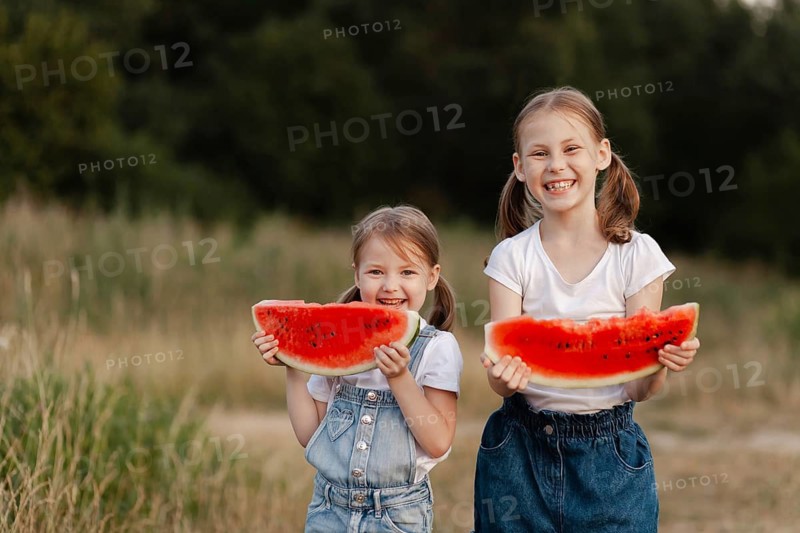 Two smiling children enjoy delicious watermelon slices on a sunny summer day outdoors. Their joy and laughter capture the essence of childhood and warm weather fun