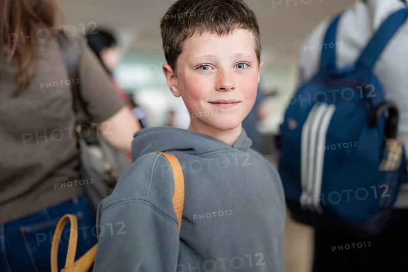 A boy with a backpack stands in a bustling airport terminal. The atmosphere is busy and dynamic, capturing the essence of modern-day travel and exploration