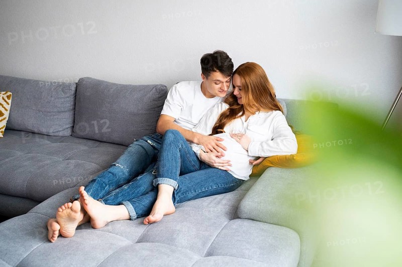 A young couple lovingly embraces on a cozy couch, celebrating their journey into parenthood. The expectant mother cradles her baby bump with joy and anticipation
