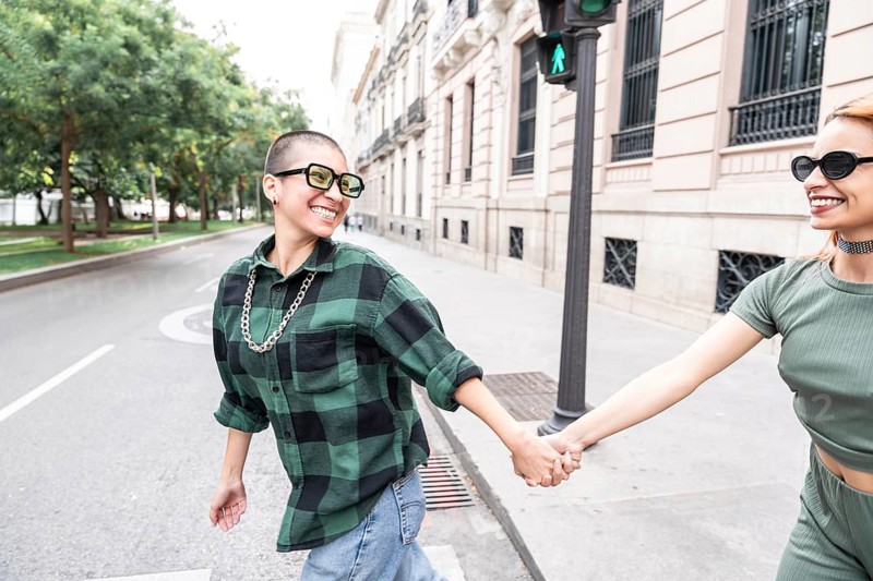 A cheerful Colombian lesbian couple holds hands while walking on a city street, symbolizing love and diversity. The image represents LGBTQIA+ pride and acceptance