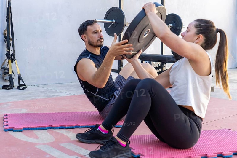 Two fitness professionals engaging in abdominal exercises with a weight plate during an invigorating outdoor training session, showcasing teamwork and dedication to health and wellness