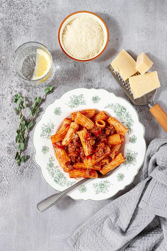 Rigatoni pasta with meat sauce and parmesan cheese on a light table, top view, homemade, no people