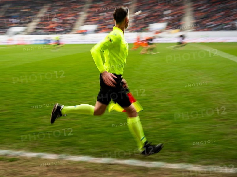 Assistant referee in a vibrant neon yellow kit running along the sideline during a professional soccer game with motion blur in Lubin, Poland