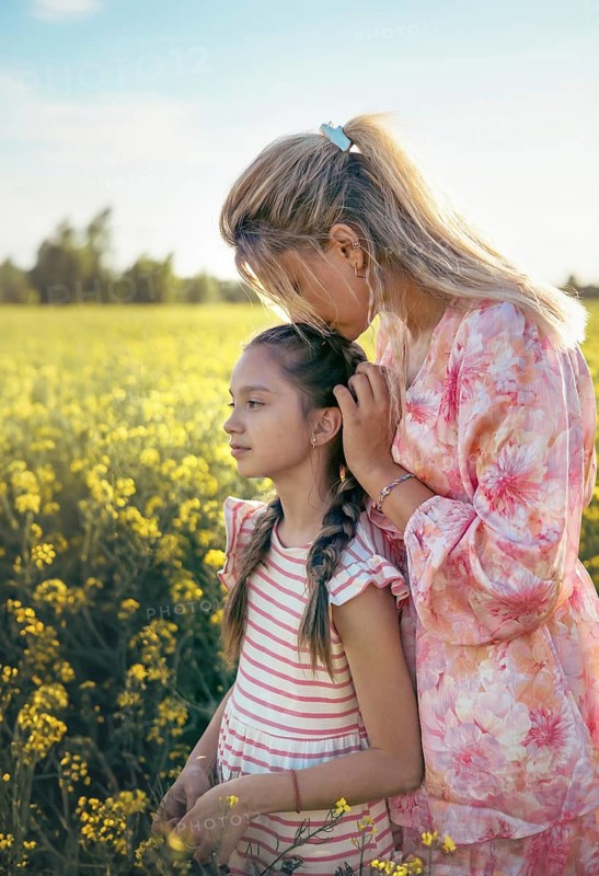 A mother and daughter spend quality time in a blooming yellow flower field, enjoying the warm sunset. The peaceful moment captures love, connection, and the beauty of nature