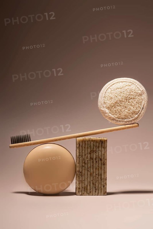 A bamboo toothbrush elegantly balances on a beige soap bar and a natural pumice stone against a smooth beige background, showcasing eco-friendly toiletries for a sustainable lifestyle
