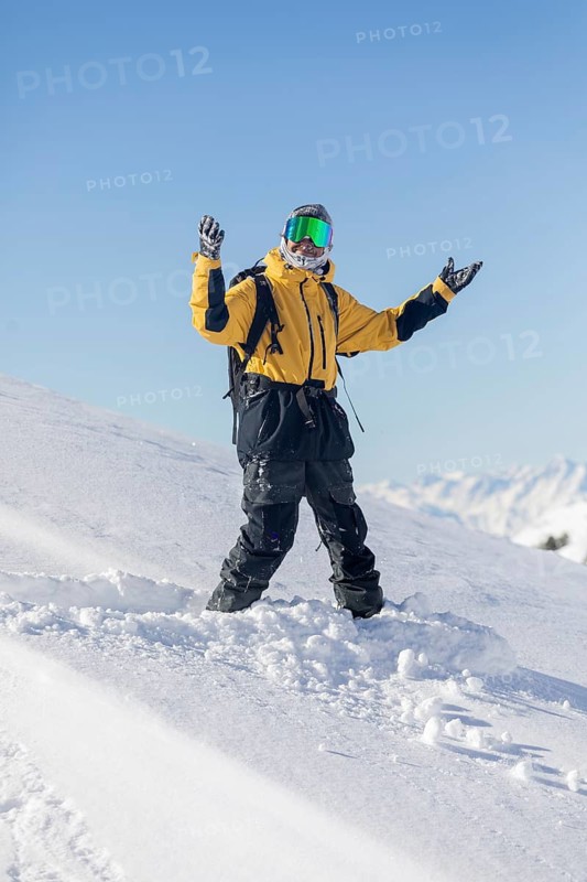 A snowboarder in a yellow jacket enjoys a sunny day on a snowy mountain slope, with clear blue skies and pristine snow underfoot, capturing the essence of winter sports