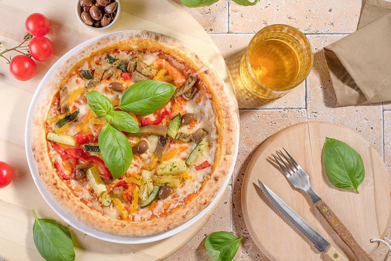 A delicious vegetarian pizza topped with fresh basil, zucchini, eggplant, and peppers. The rustic setting highlights the vibrant colors and fresh appeal of this gourmet meal