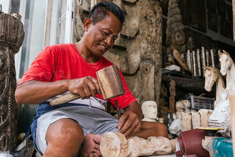 A skilled Indonesian artisan is absorbed in carving a wooden sculpture. His focused expression and handcrafted tools reflect the dedication to traditional craftsmanship